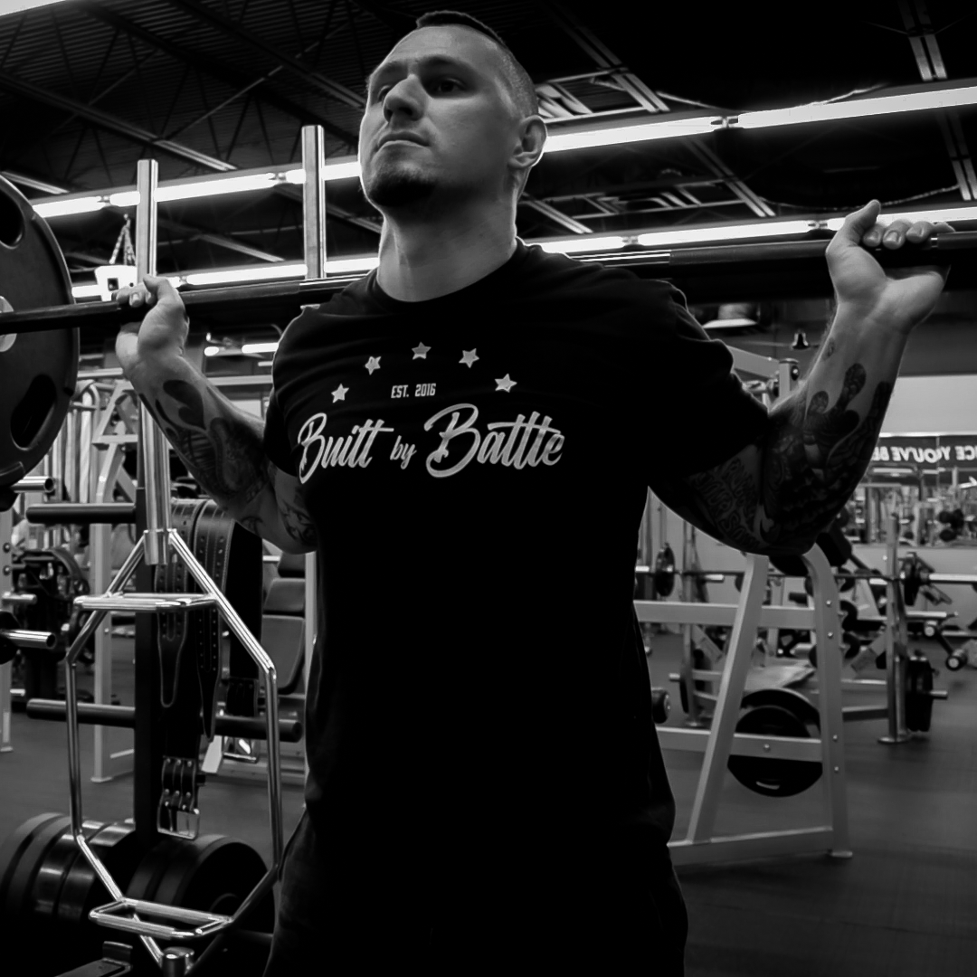 Tattooed man working out while wearing Built By Battle t-shirt